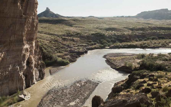 a river winds through a desert landscape with high canyon walls and mountains in the distance